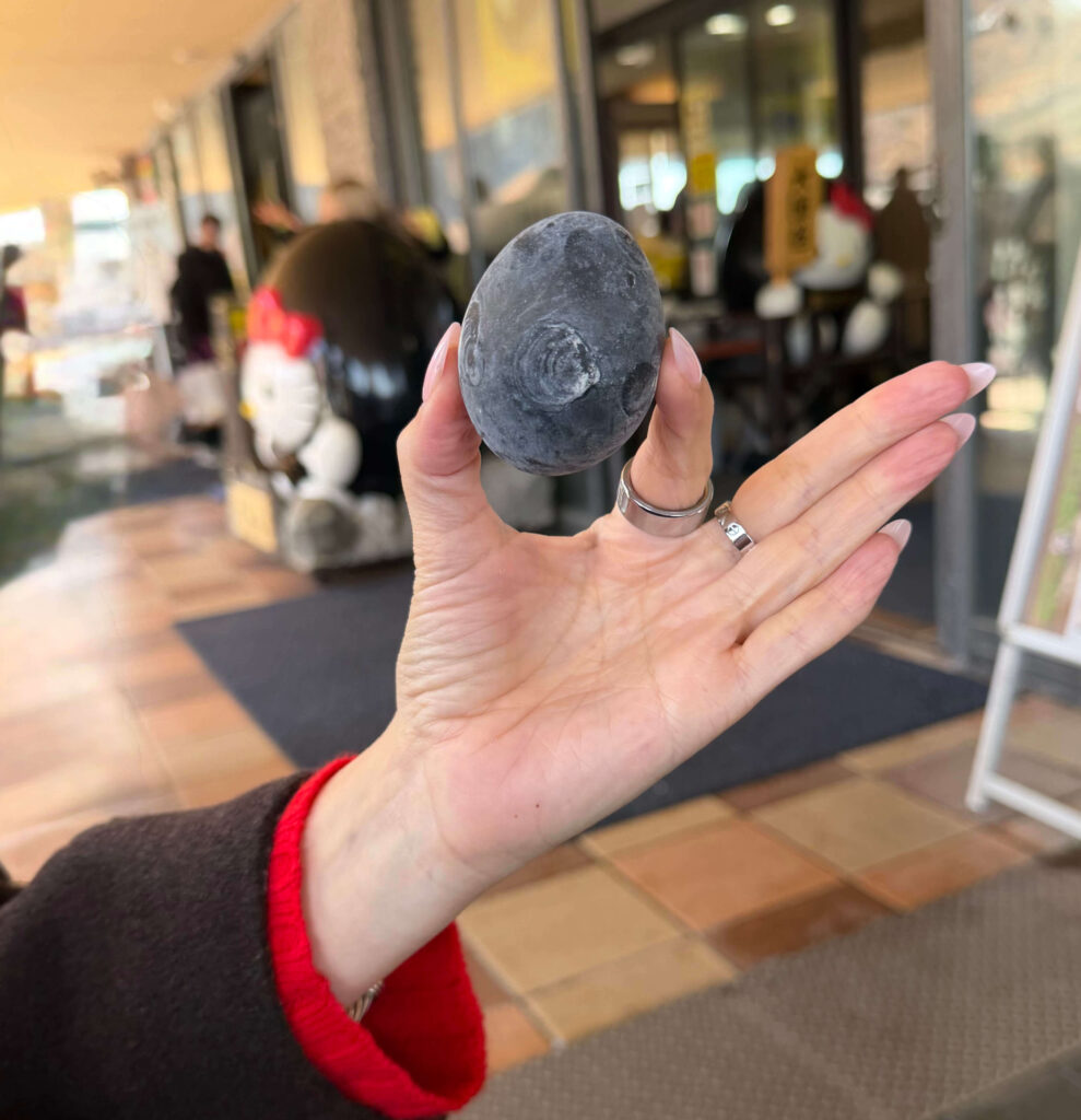 Hand holding a black egg in front of a shop at Owakudani in Hakone