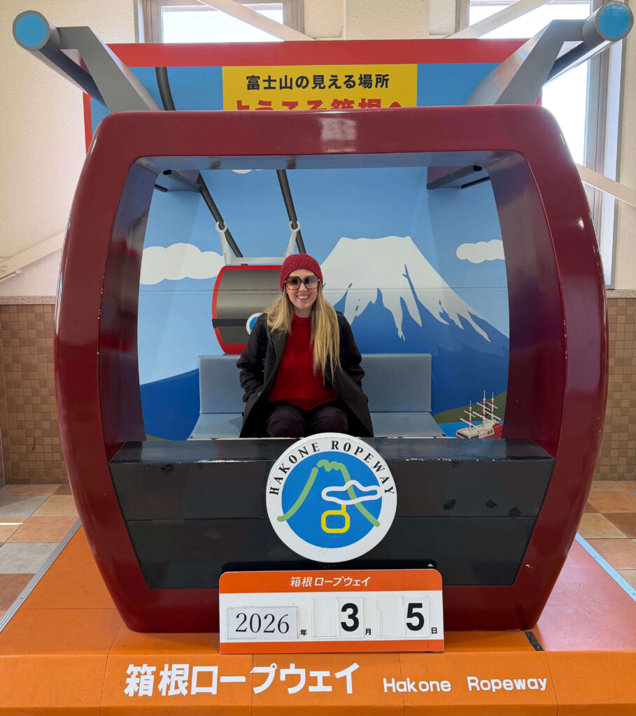 Woman in a red hat sitting in a Hakone Ropeway photo booth with a Mount Fuji mural