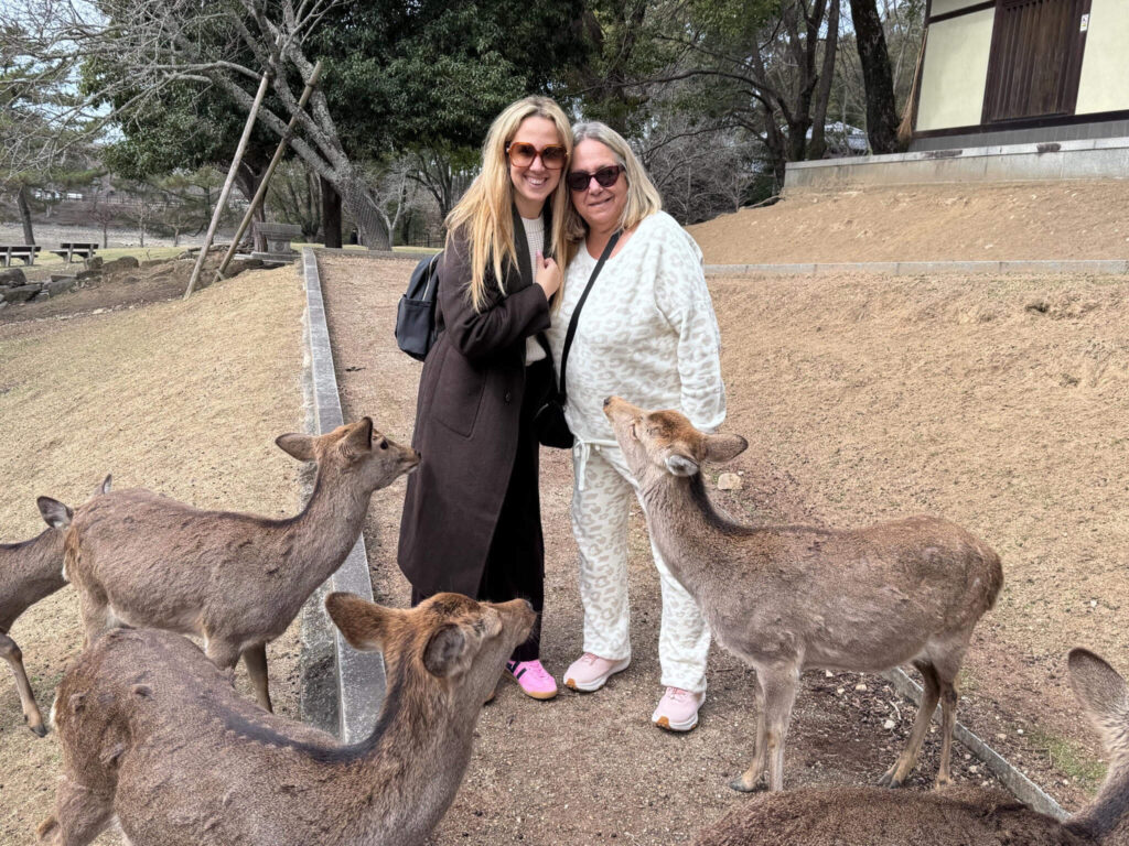 A mother and daughter posing with friendly sika deer in Nara