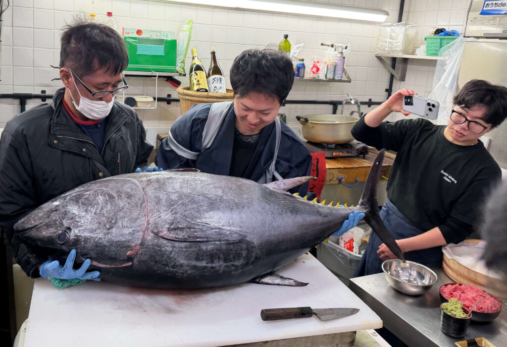Staff holding a whole tuna on a cutting board during a tuna cutting demonstration at Nishiki Market in Kyoto