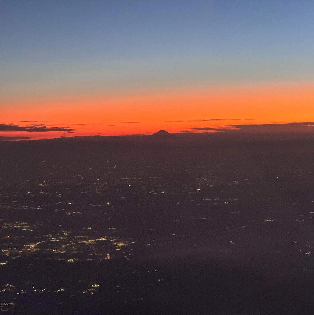 Orange and blue sunset from a plane window with a mountain silhouette on the horizon