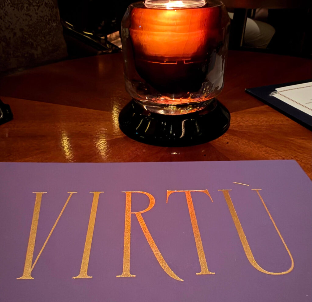 Gold lettering on a purple Virtù menu next to a glowing candle on a wooden table at the Four Seasons in Tokyo