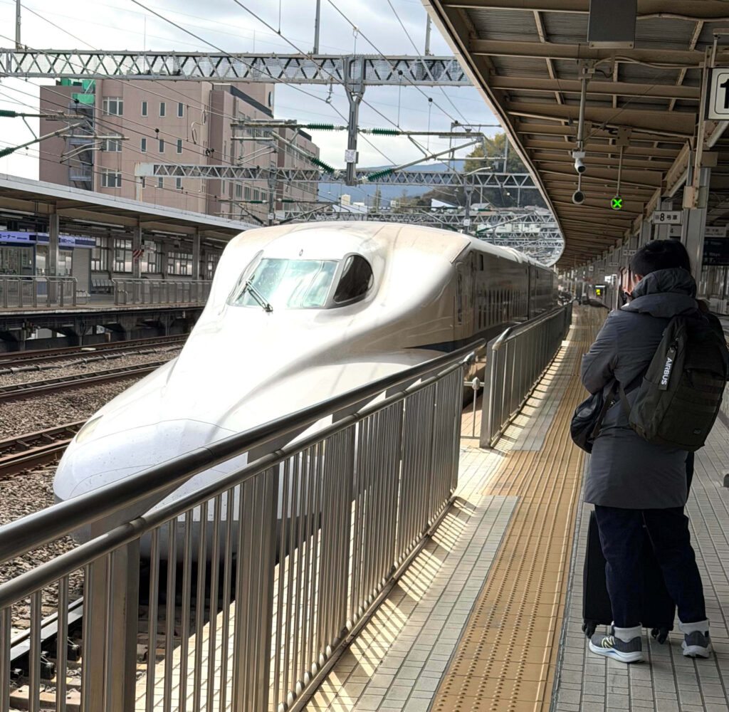 White Shinkansen bullet train waiting at a station platform with a traveler and luggage standing nearby