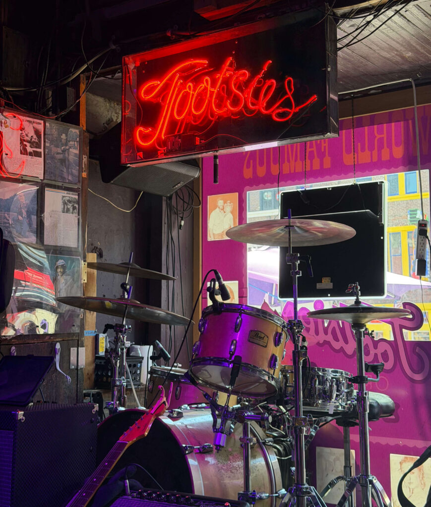 Red neon Tootsie's sign above a drum kit on stage inside Tootsie's Orchid Lounge